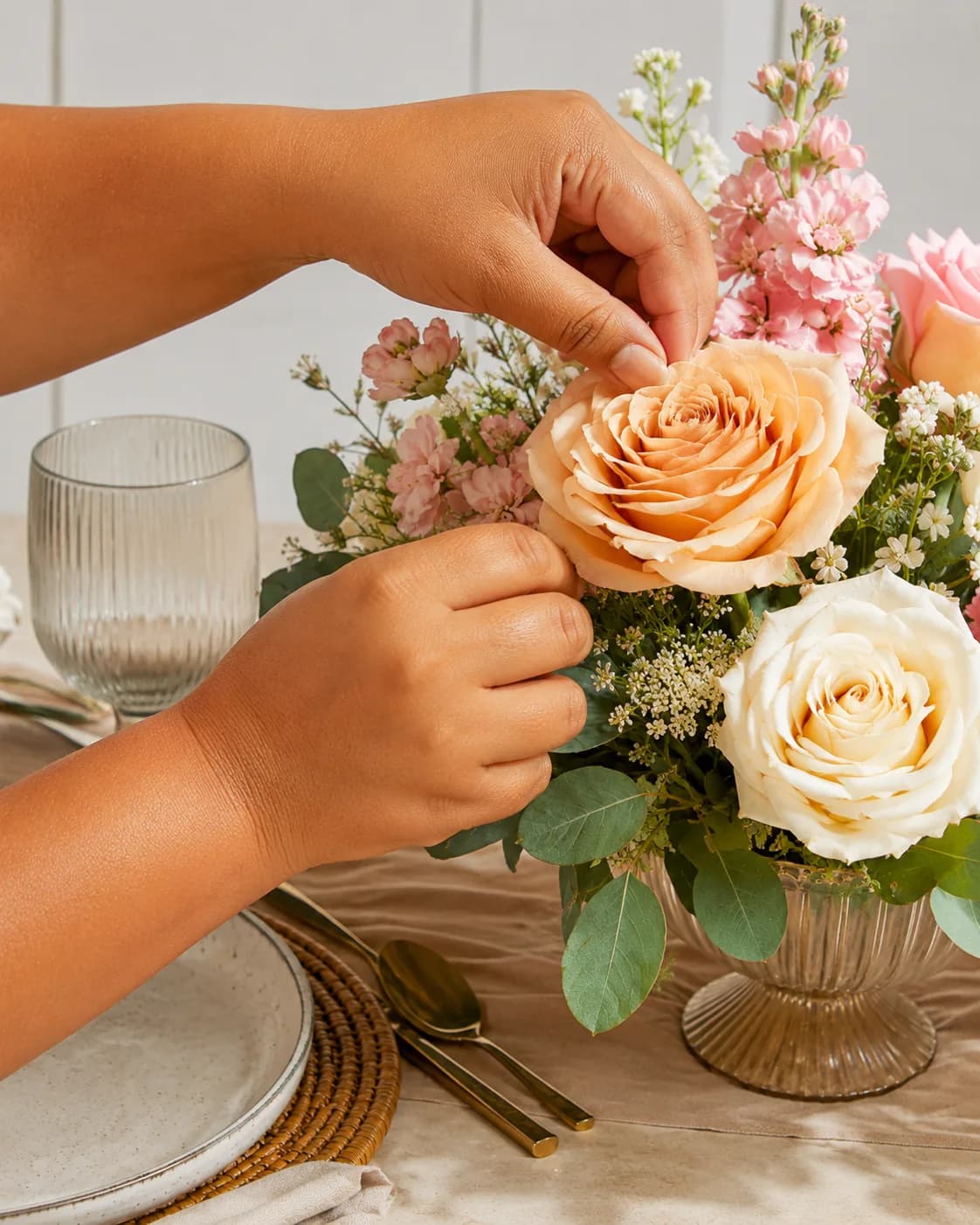 Hands arranging pink and cream flowers in a table centerpiece