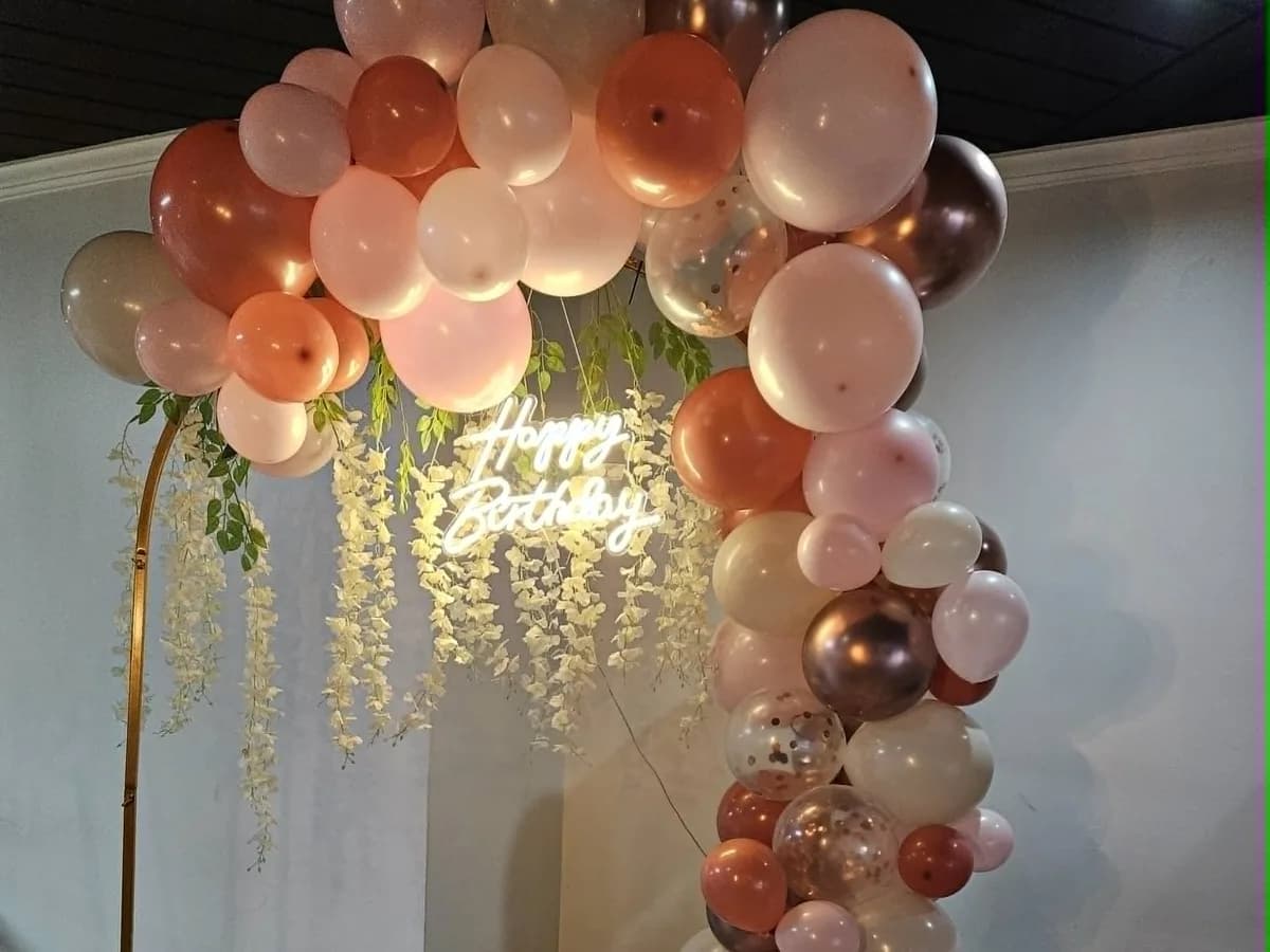 Pink and rose-gold balloon arch with a Happy Birthday sign