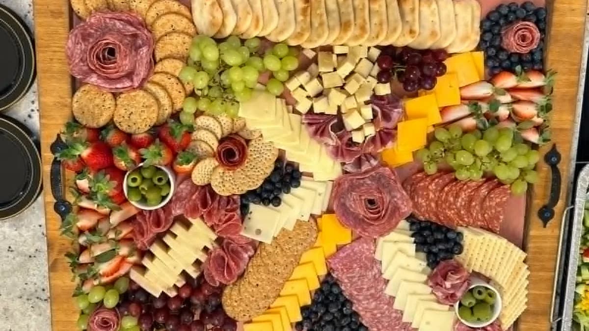 Charcuterie board arranged with fruit, cheese, crackers, and meats
