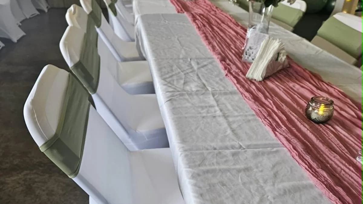 Long event table with a pink runner, covered chairs, and flowers